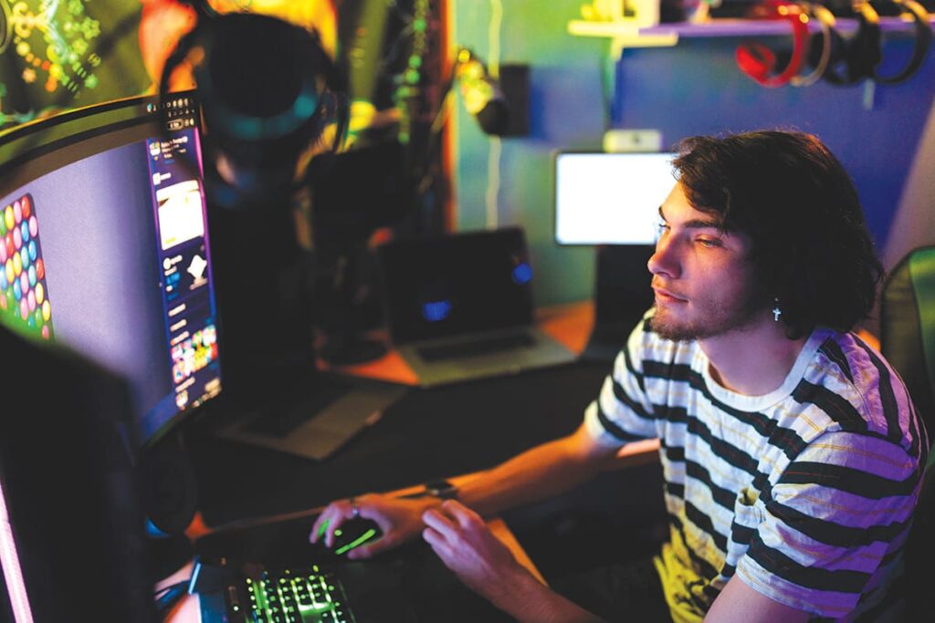 Boy playing computer games on multiple monitors.