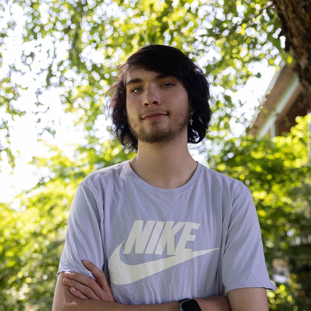 Photo of boy outdoors in gray t-shirt with arms crossed.