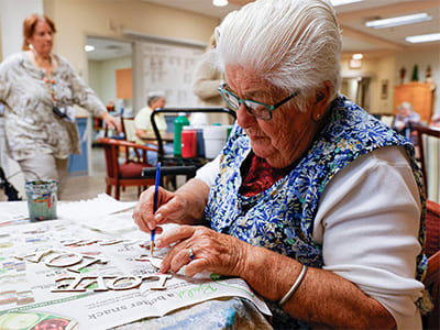 Older woman painting in a classroom.