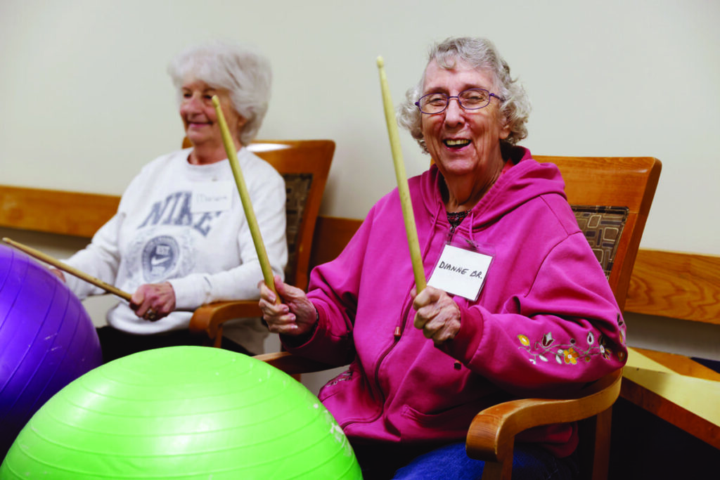 Two older woman playing drums on exercise balls. 