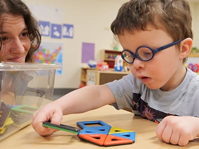 Young boy playing with crafts on a table while mom watches.